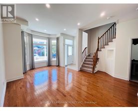 A spacious room with wooden floors and a staircase.