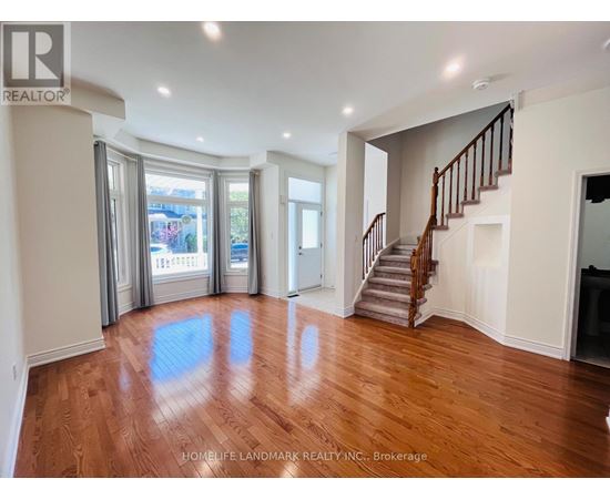 A spacious room with wooden floors and a staircase.