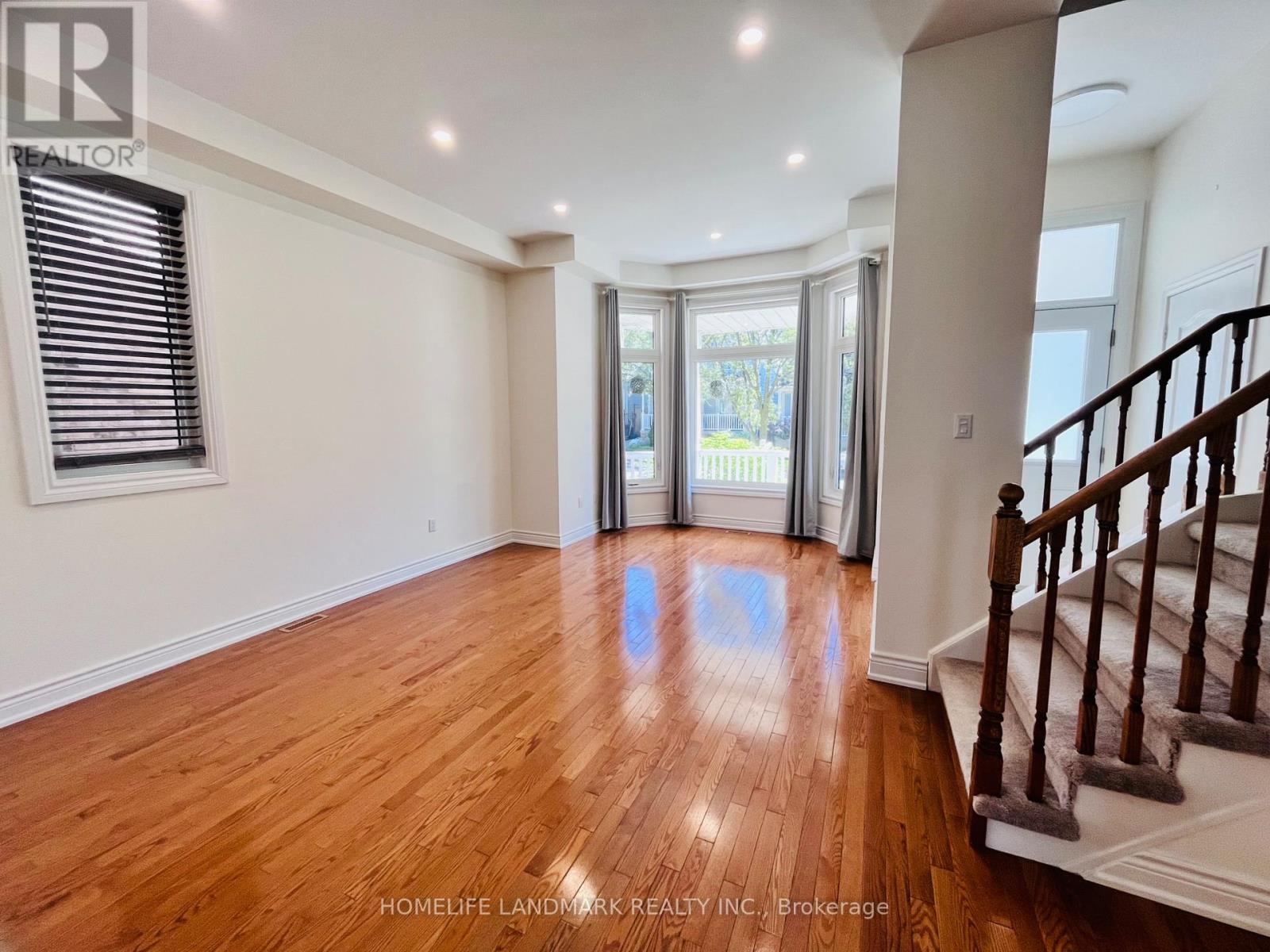 A spacious room with wooden floors and a staircase on the right side.