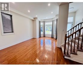 A spacious room with wooden floors and a staircase on the right side.