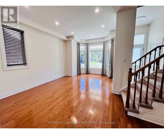 A spacious room with wooden floors and a staircase on the right side.