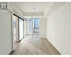 A spacious room with wooden flooring and a view of a city skyline through a glass door.