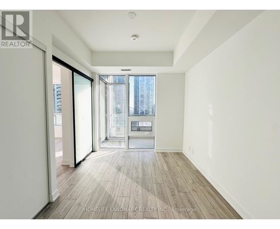 A spacious room with wooden flooring and a view of a city skyline through a glass door.