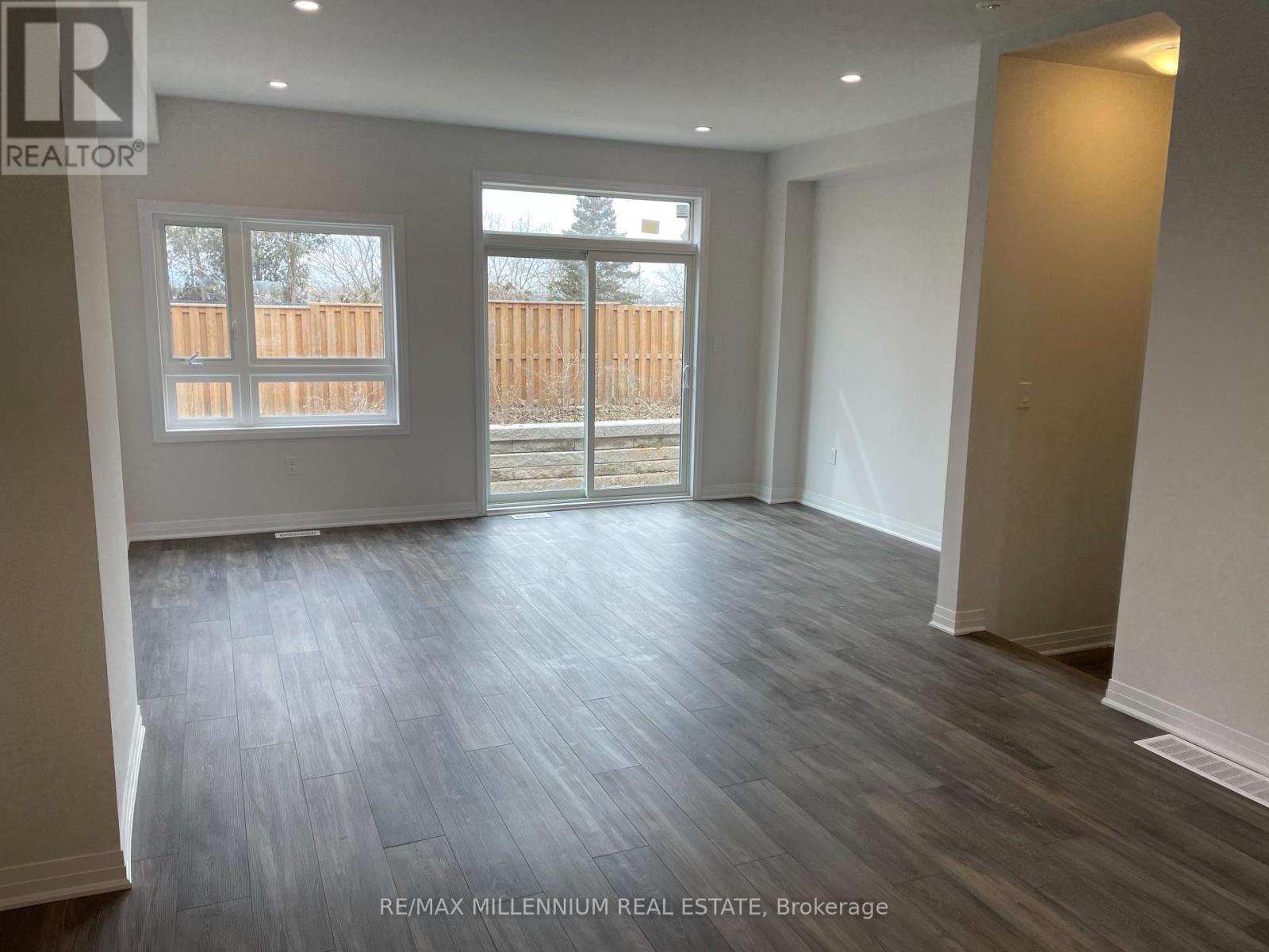 A spacious room with wooden flooring and a view of a fence through a window.