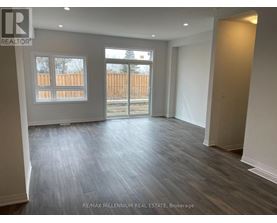 A spacious room with wooden flooring and a view of a fence through a window.