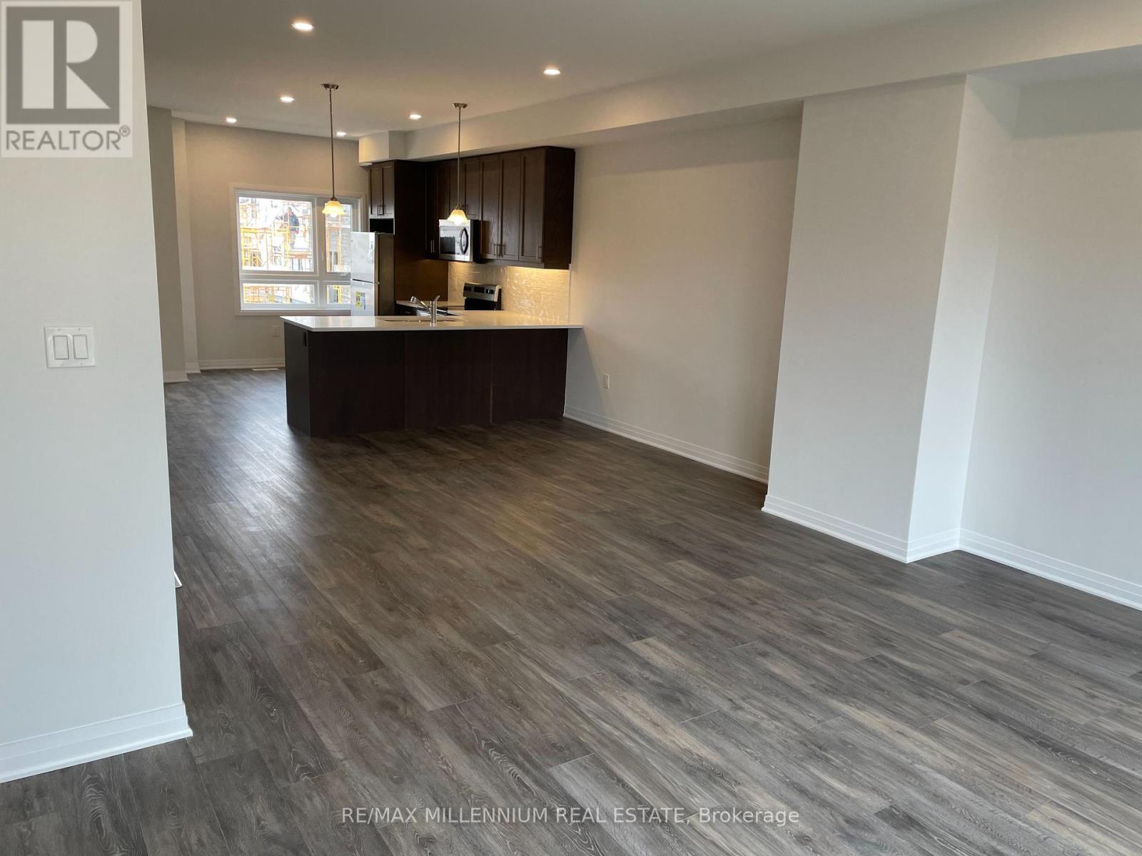 A spacious room with a wooden floor and a kitchen area with a counter and cabinets.