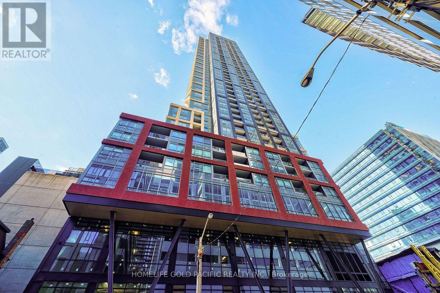 A tall building with a red and yellow facade stands in front of other buildings.
