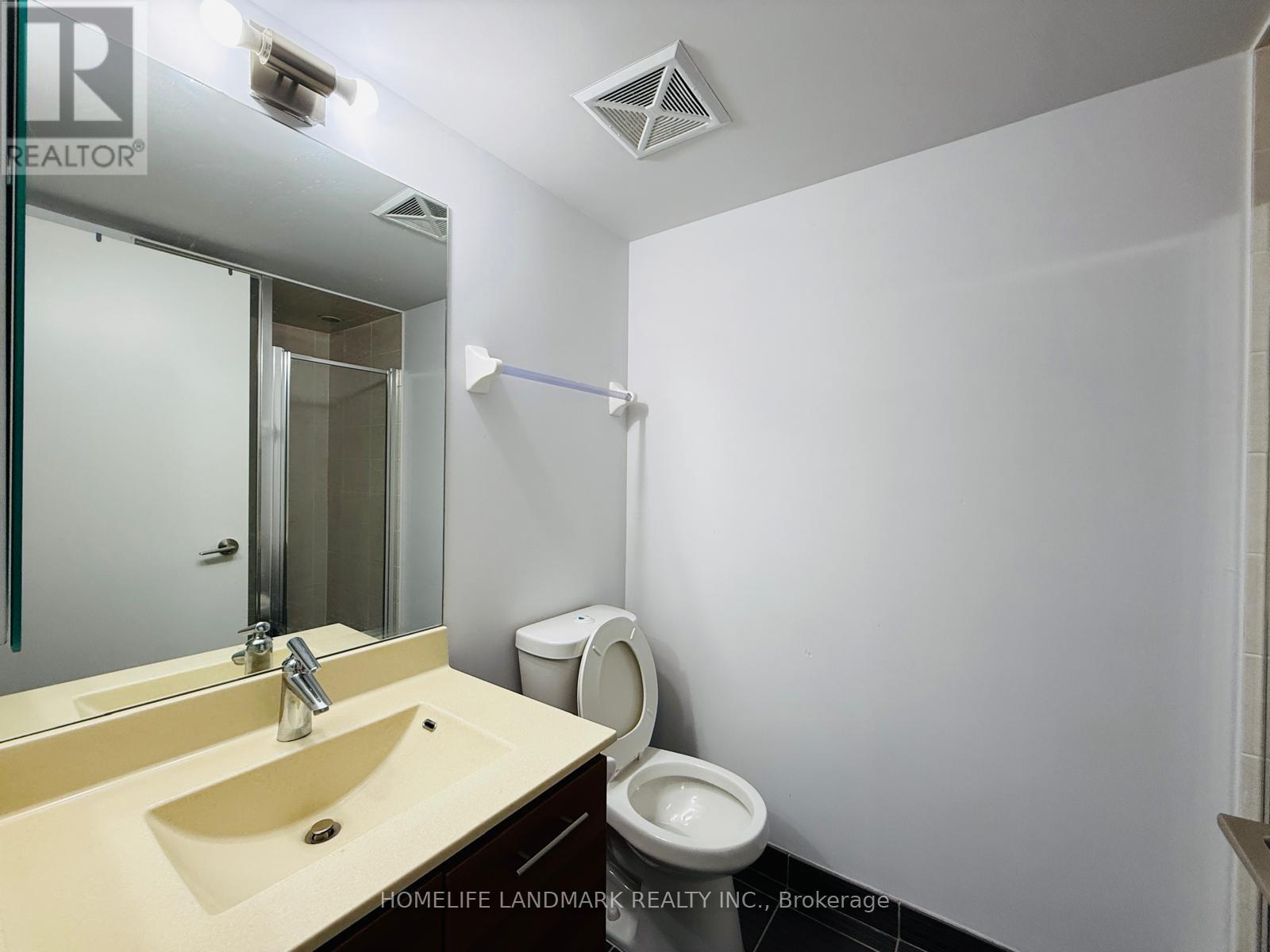 A bathroom with a sink, mirror, toilet and a white wall.