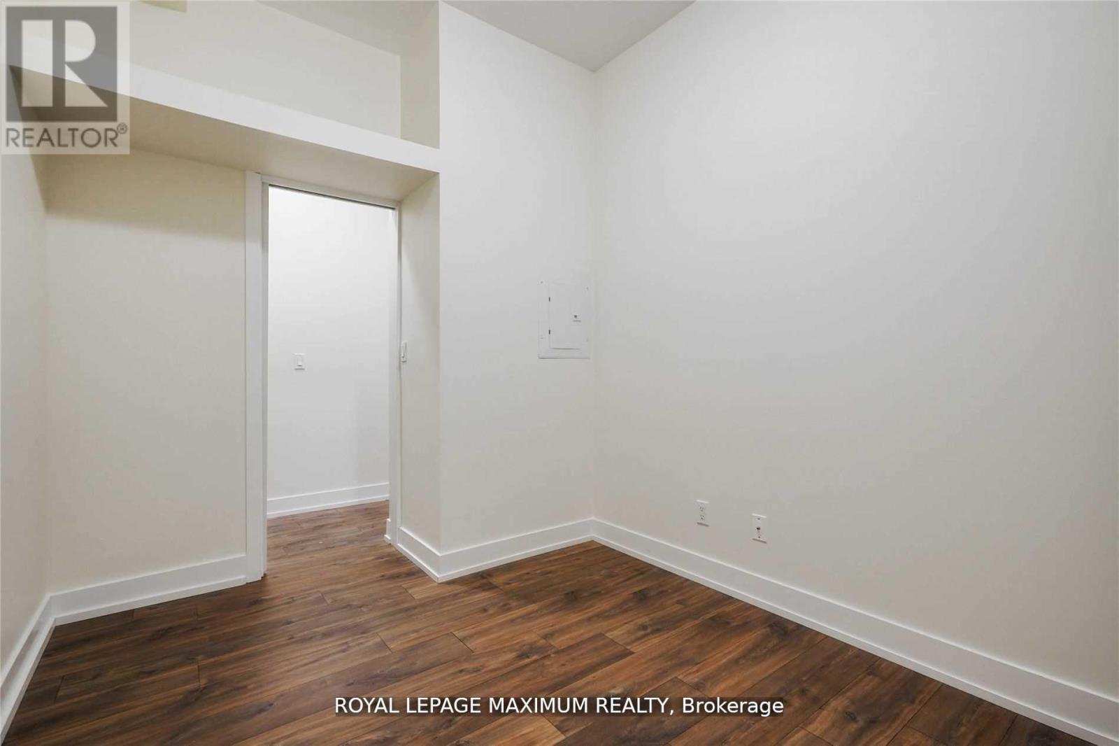 A room with white walls and wooden flooring, with a doorway leading to another room.