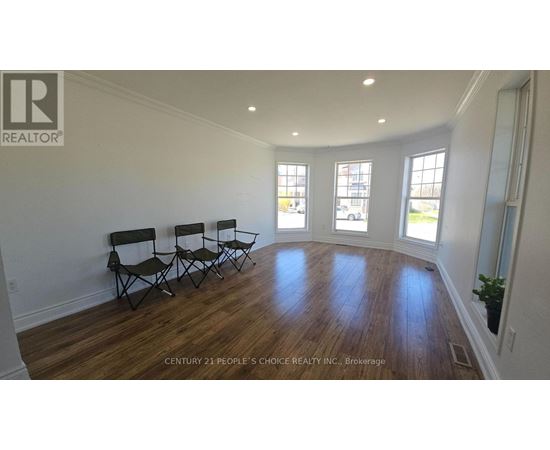A realtor logo is on a wall in a spacious room with wood floors and three chairs.