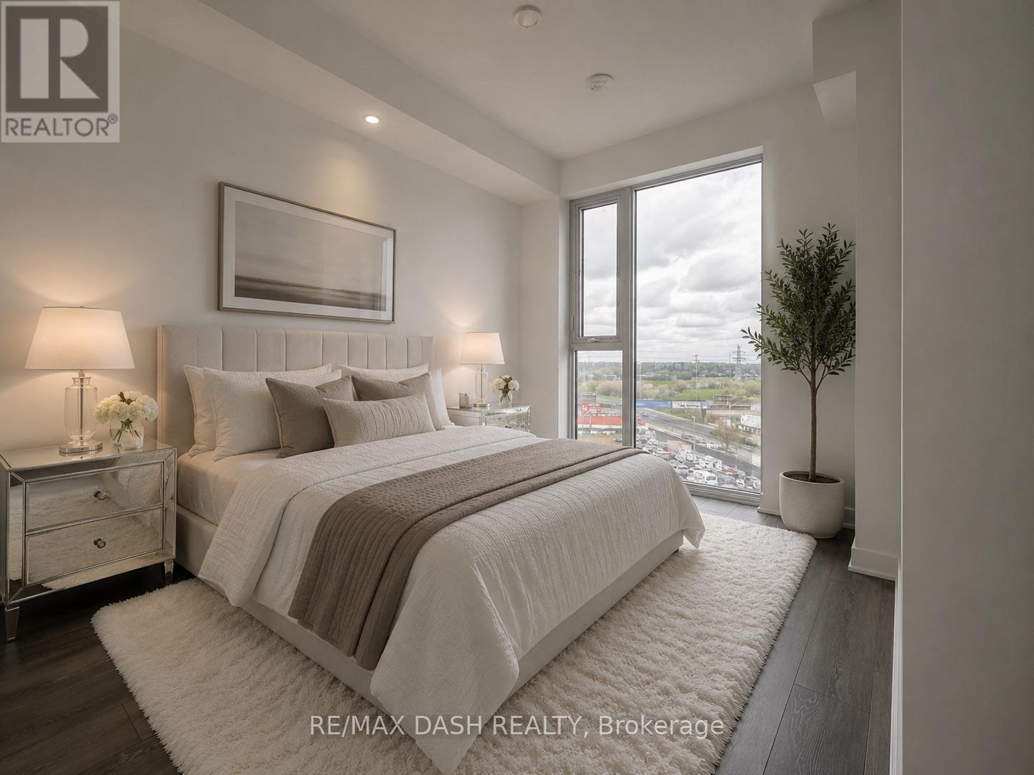 A bedroom with a large bed, a nightstand with a lamp, and a framed picture on the wall.
