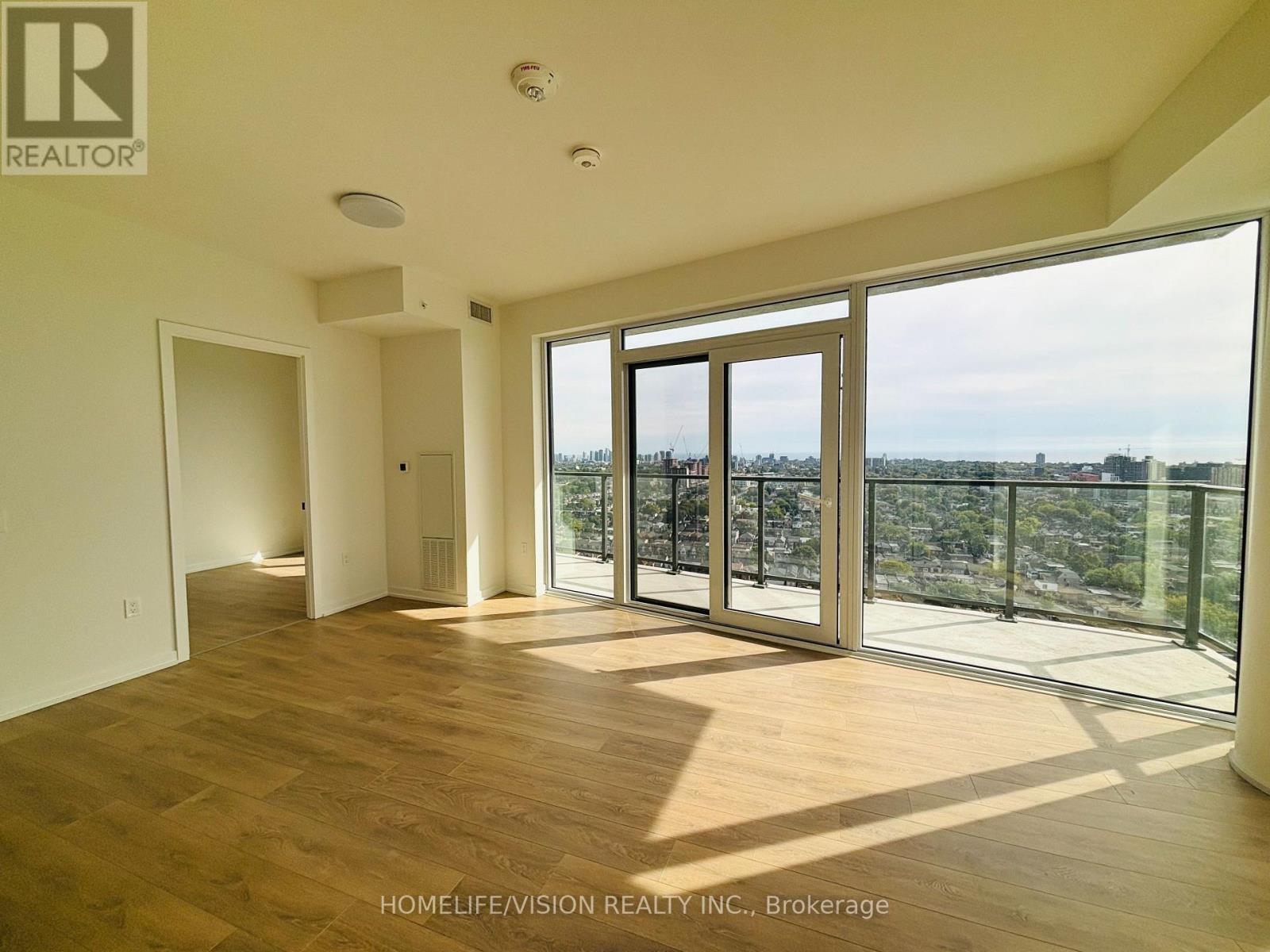A spacious room with wooden floors and large windows overlooking a cityscape.