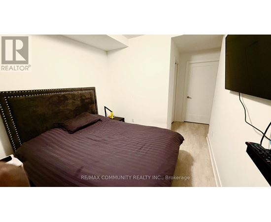 A bedroom with a bed, a flat screen TV and a brokerage sign.