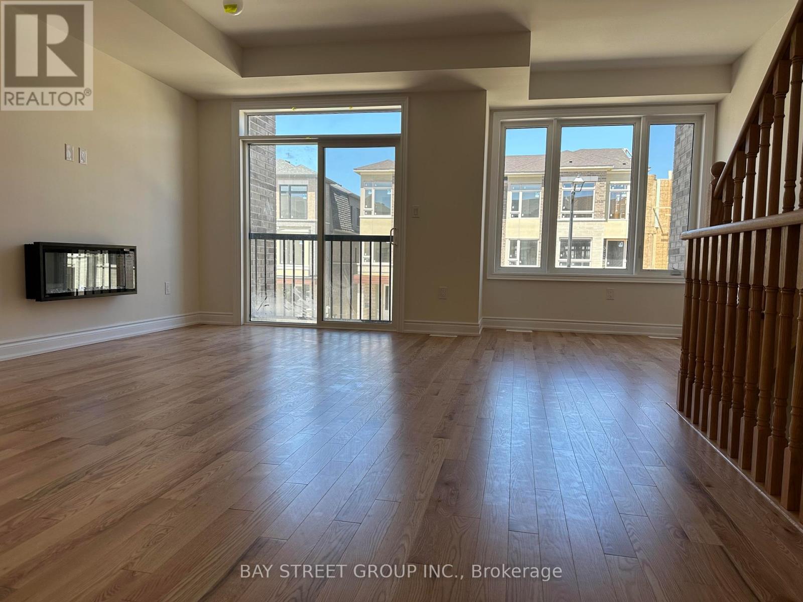 A spacious room with wooden flooring and a large window overlooking a street.