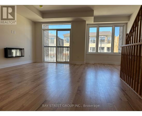 A spacious room with wooden flooring and a large window overlooking a street.
