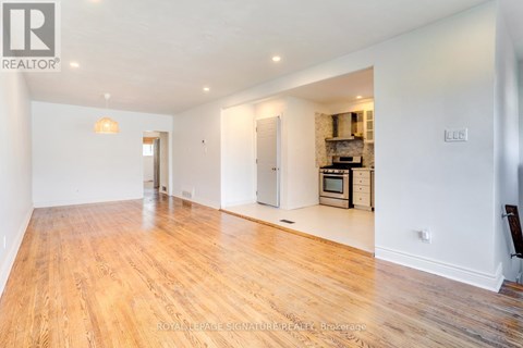 A spacious room with wooden flooring and a kitchen area in the background.