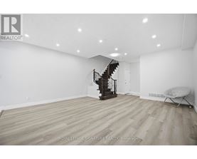 A spacious room with wooden flooring and a staircase in the background.