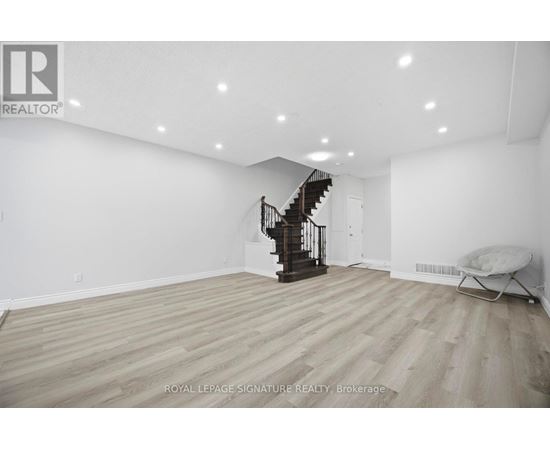 A spacious room with wooden flooring and a staircase in the background.