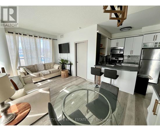 A modern living room with a glass table and a kitchen area in the background.