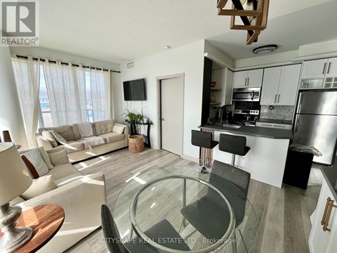 A modern living room with a glass table and a kitchen area in the background.