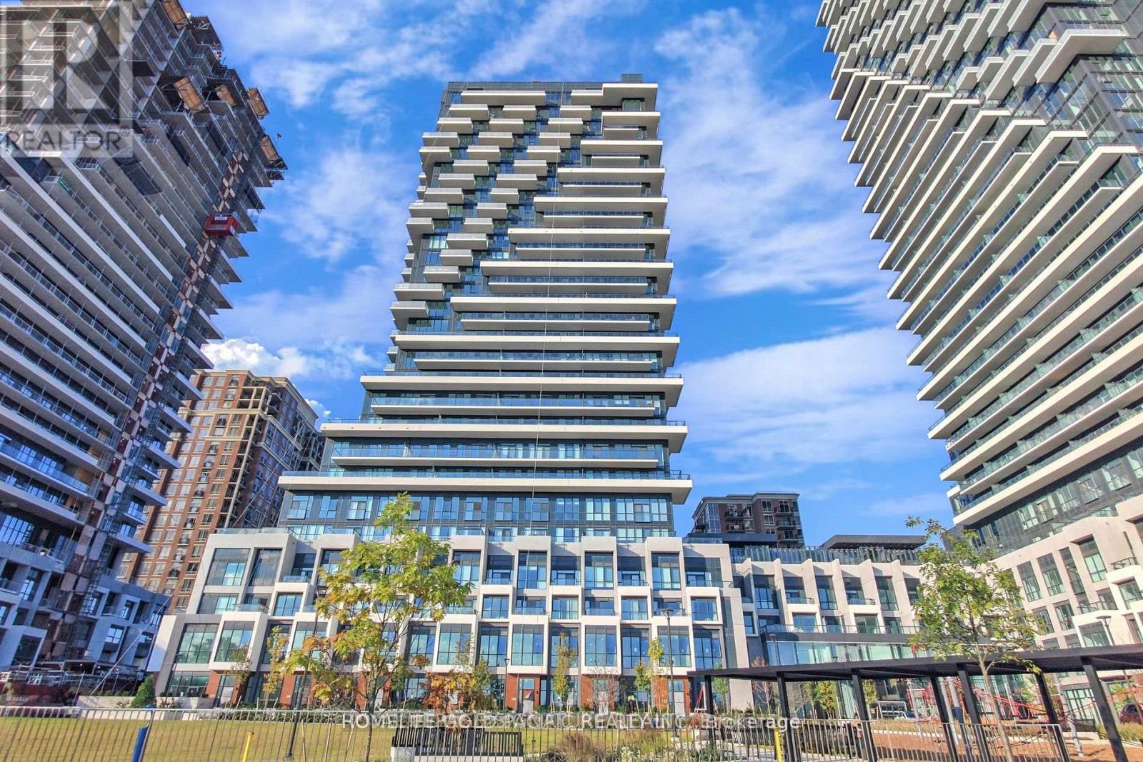 A tall, modern building with a glass facade stands in the foreground of a cityscape.