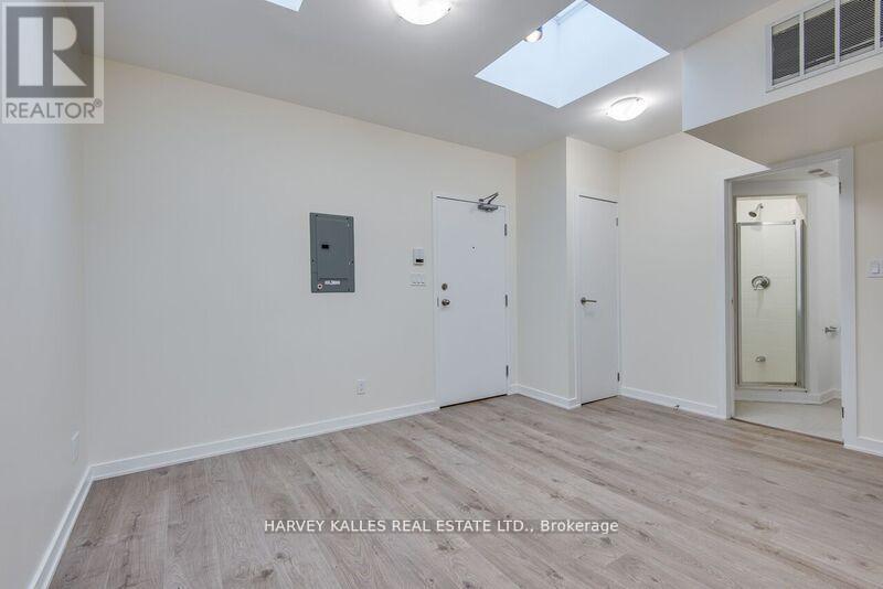 A spacious room with wood flooring and white walls, with a skylight above.
