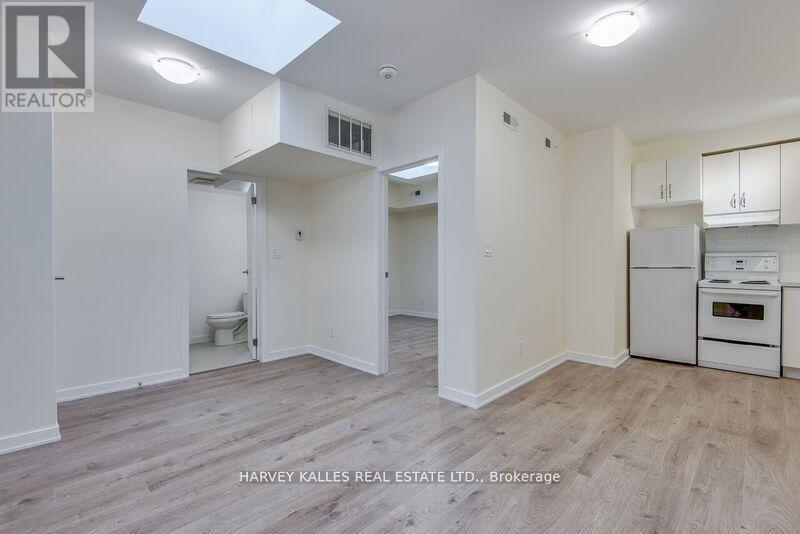 A real estate listing photo of a small, empty apartment with wood floors and white walls.