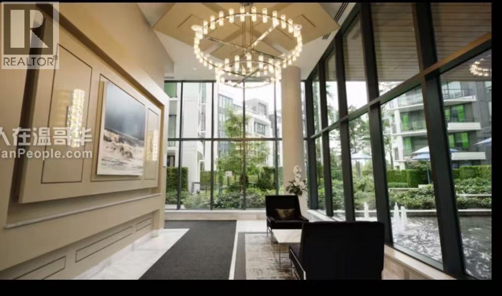 A well-lit room with a chandelier, a sofa, and a view of the outdoors through large windows.