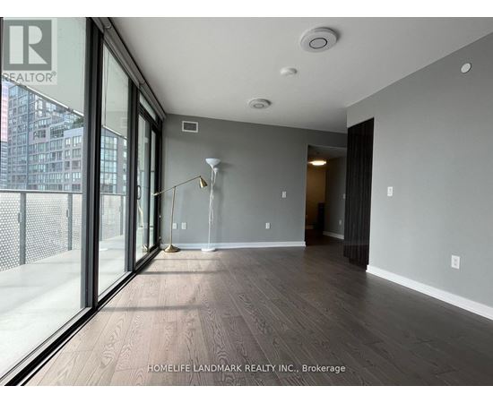 A spacious room with wooden flooring and a sliding glass door leading to a balcony.