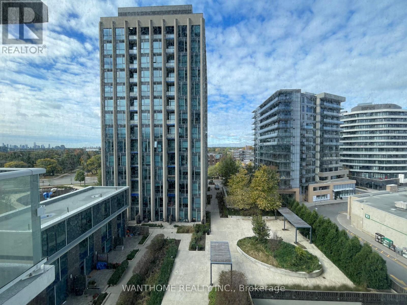 A tall building with many windows is surrounded by other buildings.