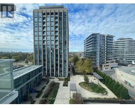 A tall building with many windows is surrounded by other buildings.