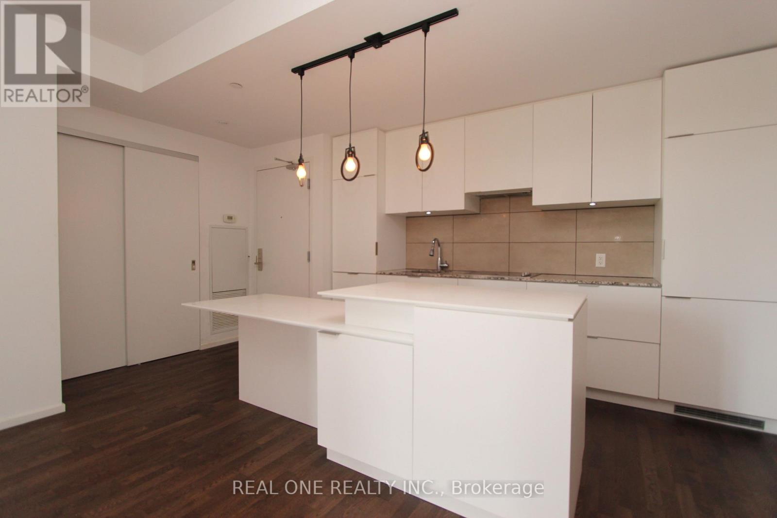A modern kitchen with white cabinets and a wooden floor.