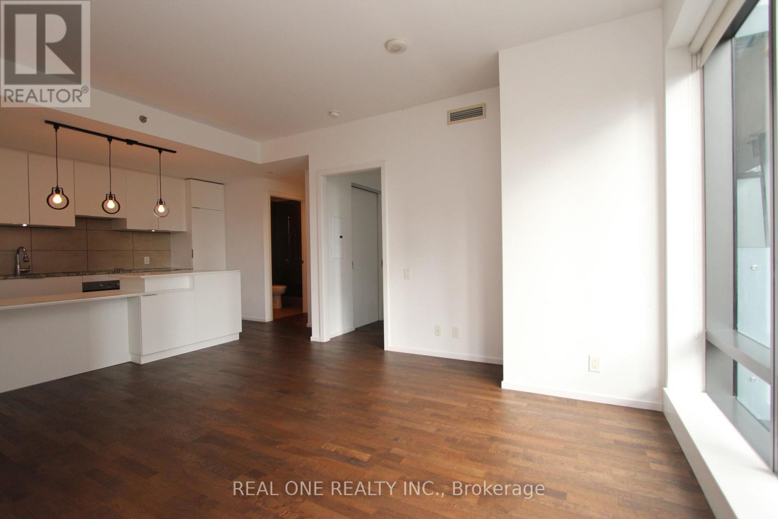 A spacious room with wooden floors and white walls, with a bar area in the corner.