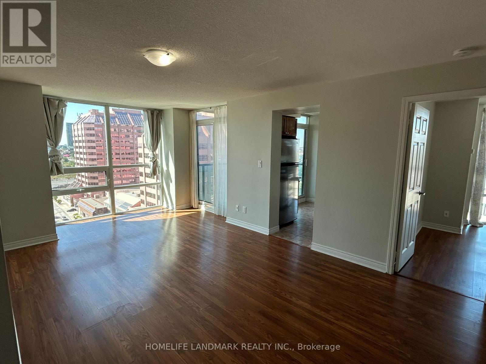 A large, empty room with wooden floors and a view of the city through the windows.