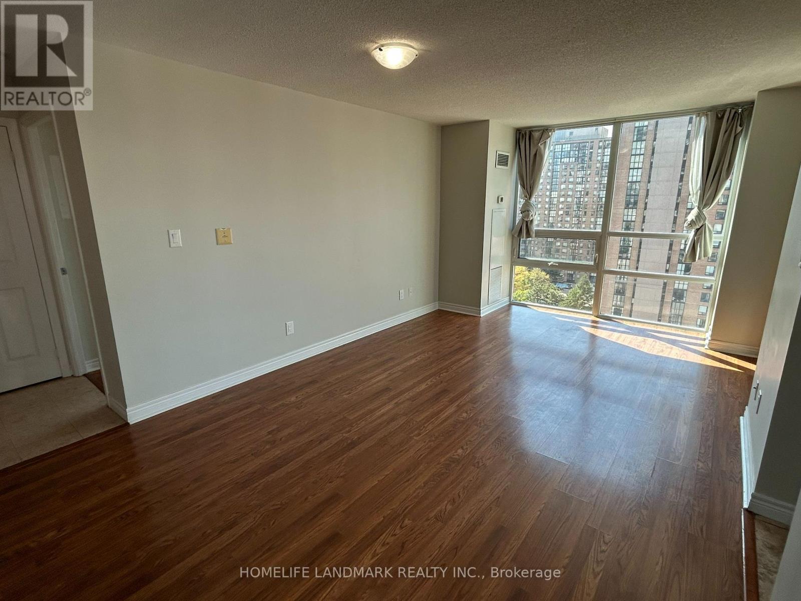 A room with wooden flooring and a large window with a view of a city.