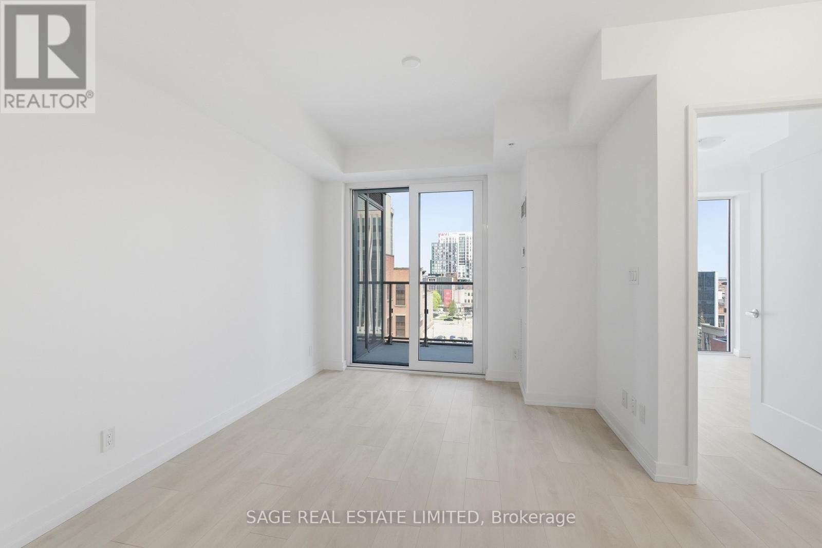 A real estate listing image of a white room with a door leading to a balcony.