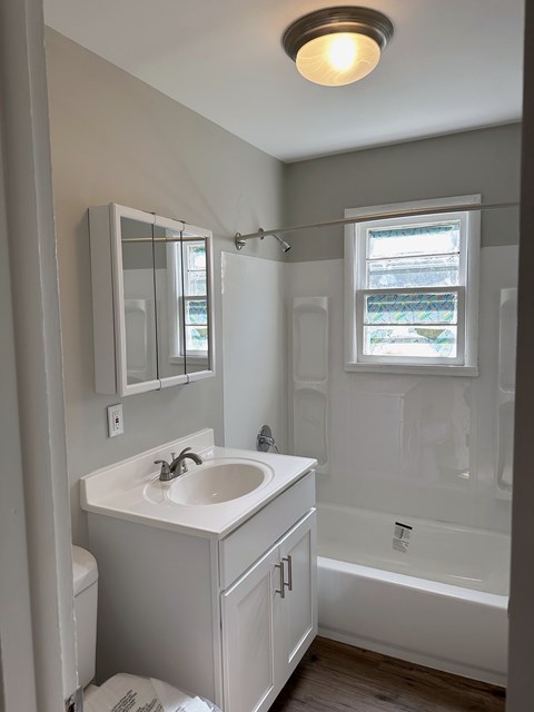 A white bathroom with a sink, mirror, and tub.