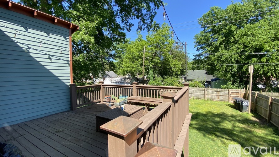 A wooden deck with a table and chairs is surrounded by a green lawn and trees.