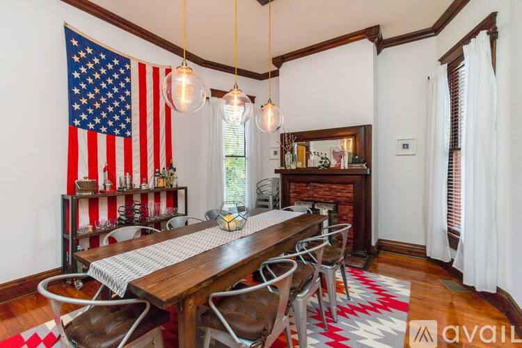 A dining room with a wooden table and chairs, a fireplace, and an American flag hanging on the wall.