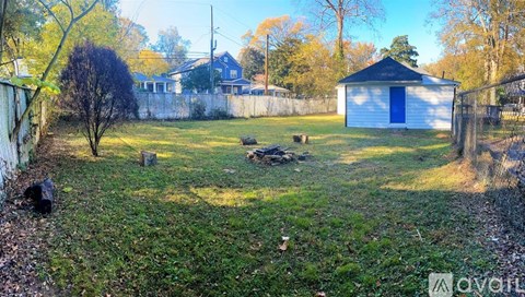 A small white shed with a blue door is situated in a grassy backyard.