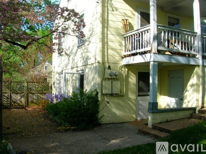 A yellow house with a balcony and a tree in front.