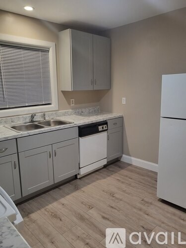 A kitchen with a white fridge, grey cabinets and a white sink.