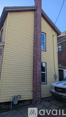 A yellow house with a red brick chimney and a white car parked in front.