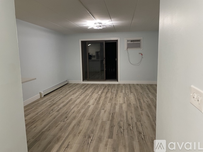 A room with wooden flooring and a white wall with a window.