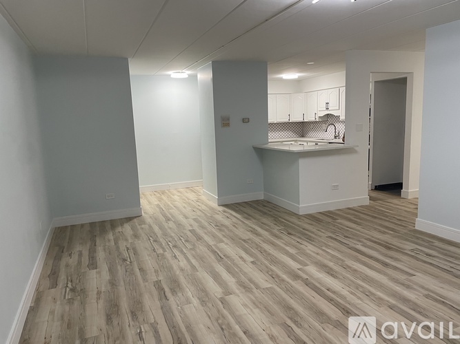 A room with wooden flooring and a kitchenette in the corner.