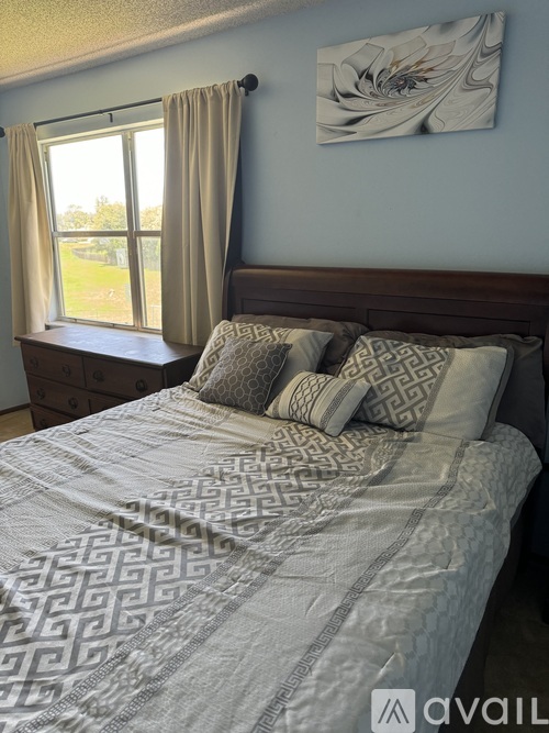 A bed with a patterned comforter and pillows in a room with a window.