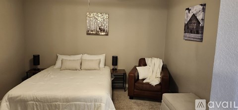 A bedroom with a white bed and a brown chair.