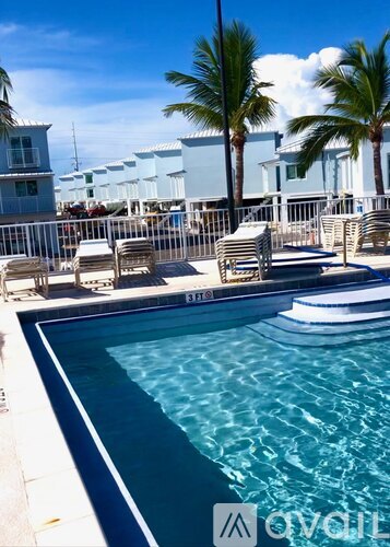 A pool with chairs and palm trees in the background.