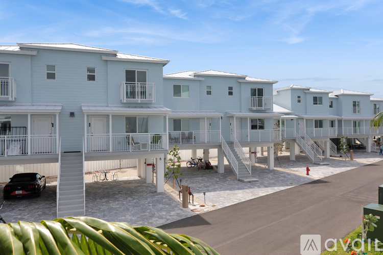 A row of white apartment buildings with balconies and a car parked in front.