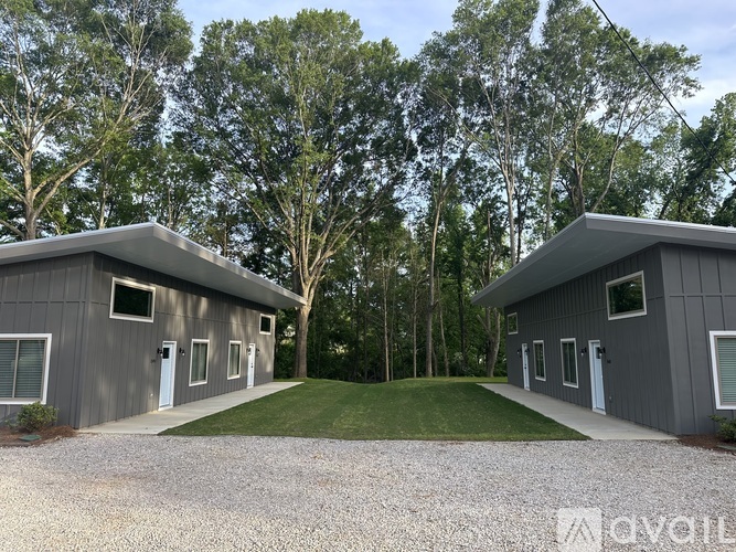 Two grey buildings with white doors and windows are surrounded by trees.